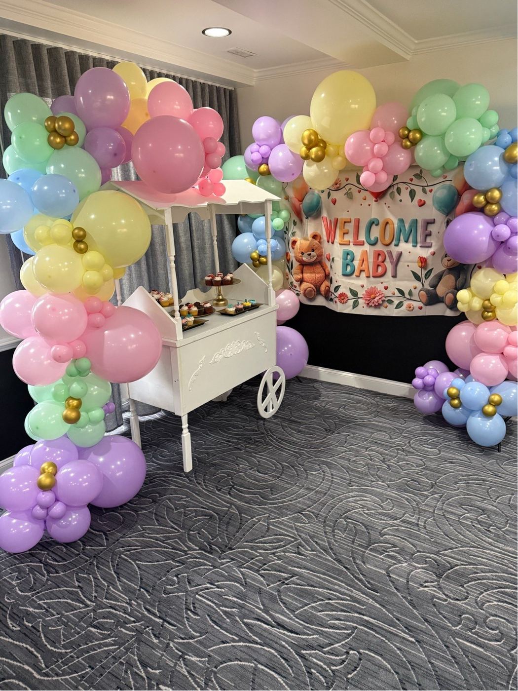 Baby shower with pastel balloon garland, welcome baby sign and a dessert cart