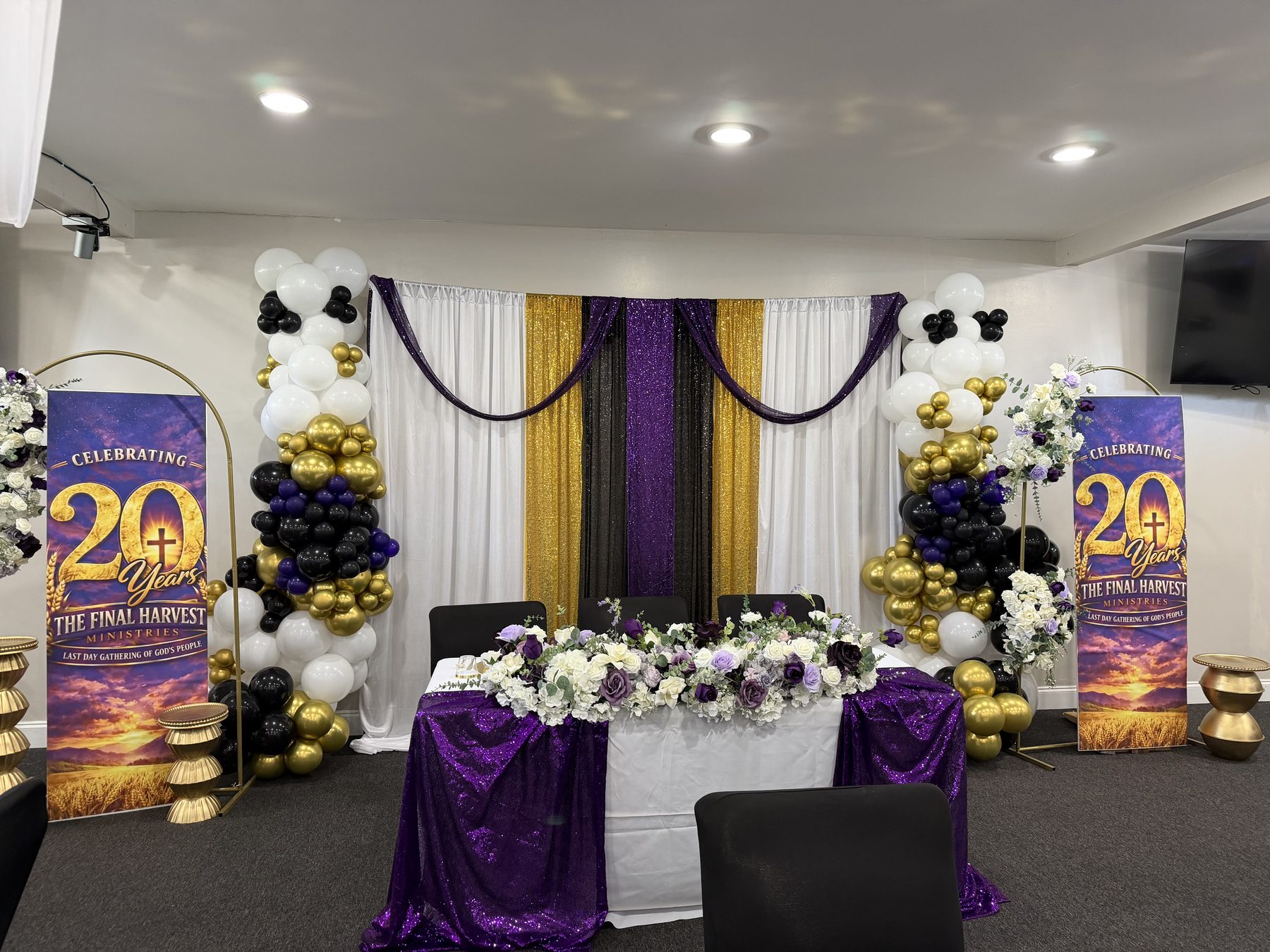 Church anniversary staged with purple, gold and black draping, balloon columns and a floral head table